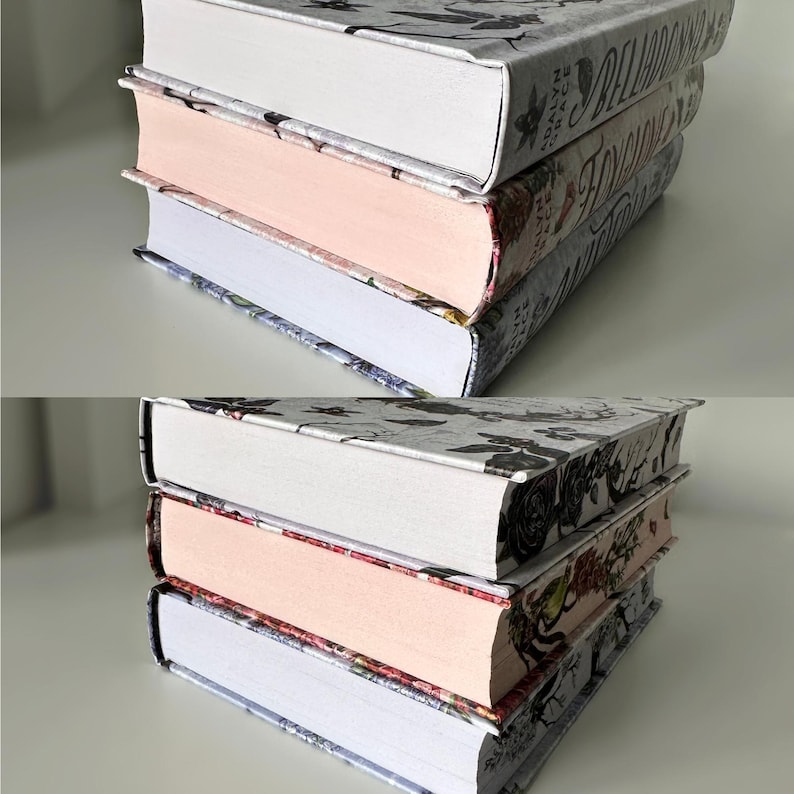 May include: Three hardcover books stacked on top of each other. The top book has a white cover with black floral designs and the text "A Ballad of Love and Glory" printed on the spine. The middle book has a pink cover with black floral designs and the text "The Hollow" printed on the spine. The bottom book has a blue cover with black floral designs and the text "The Raven Cycle" printed on the spine.