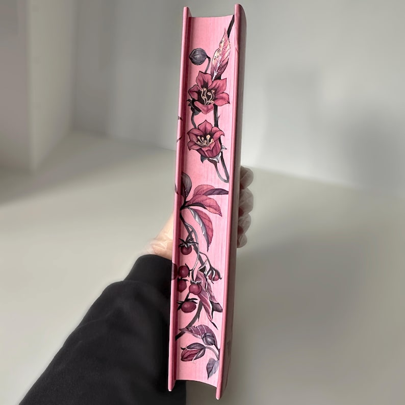May include: The spine of a pink book with a floral design. The design features pink flowers and leaves on a pink background.