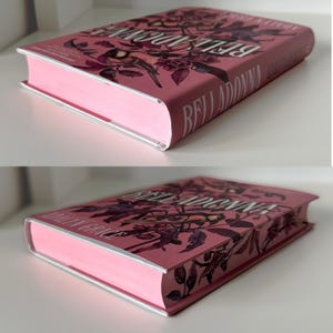 May include: A pink hardcover book with the title "BELLADONNA" in white lettering. The cover features a floral design with a bird.