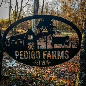 May include: Black metal farm sign with an oval frame. The sign features a barn, tree, cow, calf, and the words "PEDIGO FARMS - EST 1975-". The sign is set against a backdrop of fall foliage.