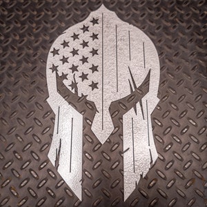 May include: A silver metal Spartan helmet with an American flag design. The helmet is on a textured black surface.