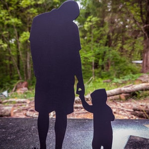 Pu&ograve; includere: Silhouette in metallo nero di un padre e un figlio che si tengono per mano. La silhouette &egrave; in piedi su una base nera.