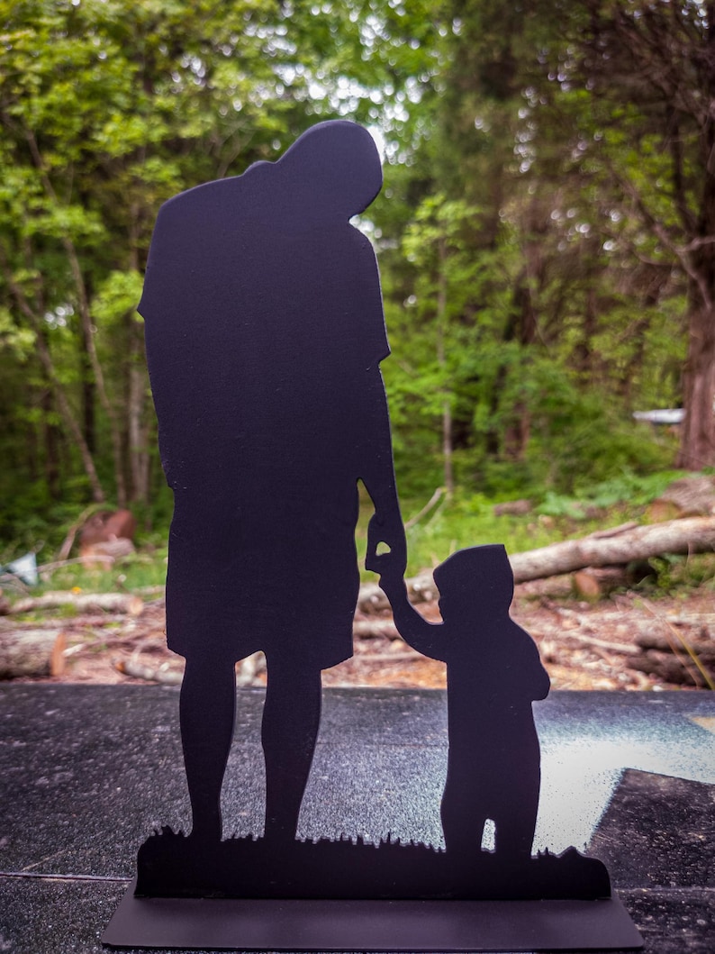 Pu&ograve; includere: Silhouette in metallo nero di un padre e un figlio che si tengono per mano. La silhouette &egrave; in piedi su una base nera.