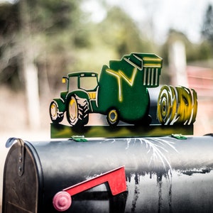 May include: A green metal mailbox with a red flag and a metal tractor cutout on top. The tractor is pulling a round bale of hay.