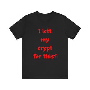 以下が含まれることがあります： 胸の中央にゴシック体の赤い文字で「I left my crypt for this?」とプリントされた黒い半袖Tシャツ。クルーネックで、標準的なフィット感とストレートな裾が特徴の衣類です。