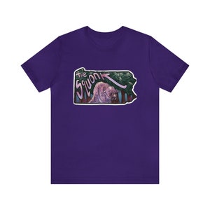 May include: Purple t-shirt with a graphic of the Pennsylvania state outline featuring a pink creature labeled "The Squonk" in a pink and white font.