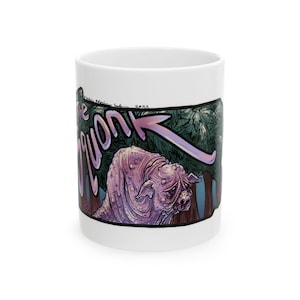 May include: White ceramic mug with a cartoon illustration of a pink creature with a snout and large ears in a forest setting. The text "The Quonk" is written in a stylized font with an arrow pointing to the creature.