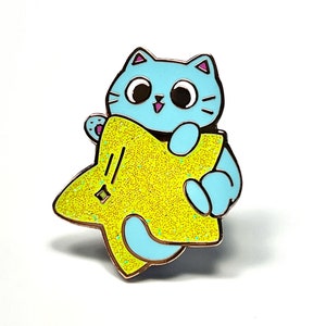 May include: A blue cat with pink ears and a big smile is holding a yellow star with glitter. The star has a small white star in the centre.