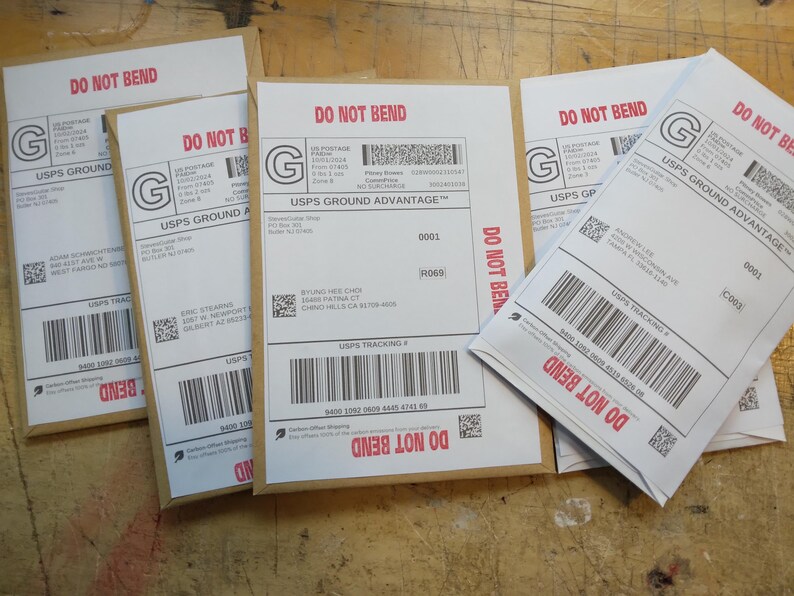 May include: Four white envelopes with brown paper backing. Each envelope has a USPS Ground Advantage label with a tracking number, a red "DO NOT BEND" warning, and a green "G" logo. The text "USPS Ground Advantage" is printed on each label.