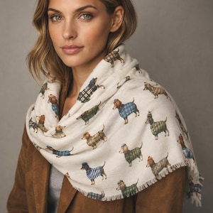 May include: An off-white scarf featuring a repeating pattern of dachshunds wearing various sweaters, hats, and scarves in shades of blue, green, and brown. The lightweight fabric has a soft texture and finished edges with a subtle fringe detail.