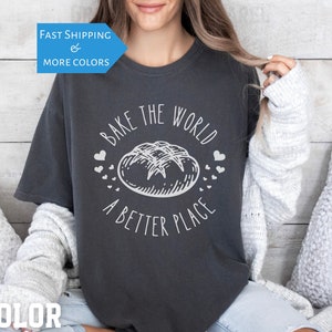 Peut inclure: Un t-shirt gris foncé avec un motif blanc représentant un pain et le texte "Bake the world a better place".