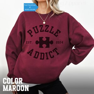 May include: Maroon sweatshirt with a black graphic that says "Puzzle Addict" with a puzzle piece in the center and "Est. 2024" underneath.