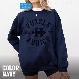 May include: Navy blue sweatshirt with a black graphic of a puzzle piece and the text "PUZZLE ADDICT EST. 2024".
