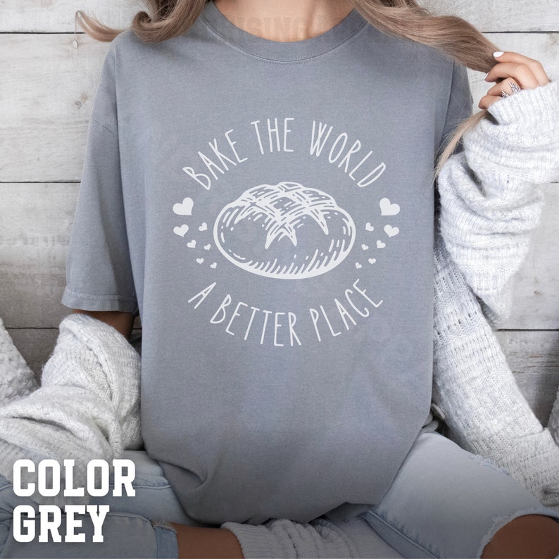 May include: A grey t-shirt with a white graphic that says "Bake the world a better place" with a drawing of a loaf of bread and hearts.
