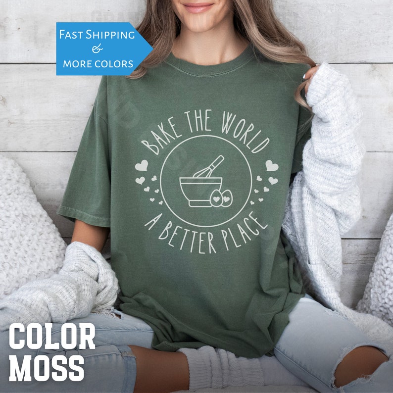May include: A green t-shirt with the text "Bake the World a Better Place" in white. The design includes a mixing bowl, whisk, and eggs.