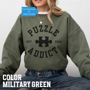 May include: A green sweatshirt with black text that reads "PUZZLE ADDICT EST. 2024" with a puzzle piece graphic in the center.