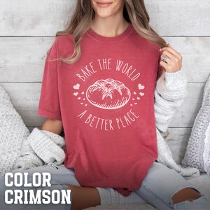 May include: A crimson t-shirt with the text "Bake the world a better place" and a drawing of a loaf of bread with hearts around it.
