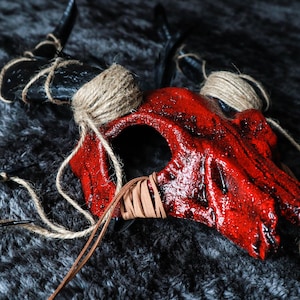 May include: A red and black skull mask with horns, wrapped in twine and leather straps.