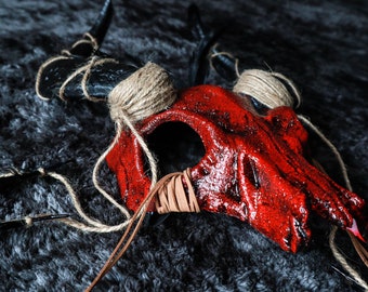 May include: A red and black skull mask with horns, wrapped in twine and leather straps.