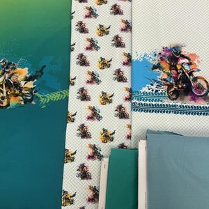 Könnte beinhalten: Stoffbahnen mit Motocross-Designs. Eine Bahn ist türkis mit einer Motocross-Fahrer-Grafik und Reifenspuren. Eine weitere Bahn ist weiß mit einem sich wiederholenden Muster von Motocross-Fahrern. Eine dritte Bahn ist weiß mit einer Motocross-Fahrer-Grafik und Farbspritzern.