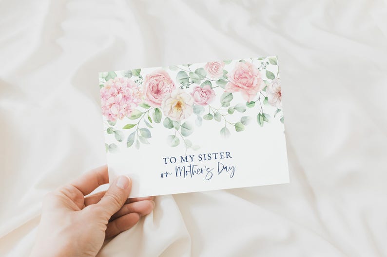 Puede incluir: Una tarjeta de felicitaci&oacute;n con un dise&ntilde;o floral con rosas rosas e hortensias, con follaje verde. La tarjeta dice "TO MY SISTER on Mother's Day" en una elegante escritura azul marino. La tarjeta se sostiene sobre un fondo blanco.