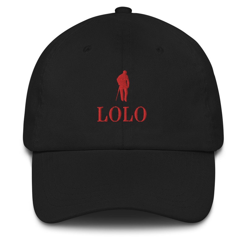 May include: Black baseball cap with a curved brim. The cap features red embroidered text that reads "LOLO" below a red embroidered silhouette of a person holding a staff. The cap is made of a soft fabric.