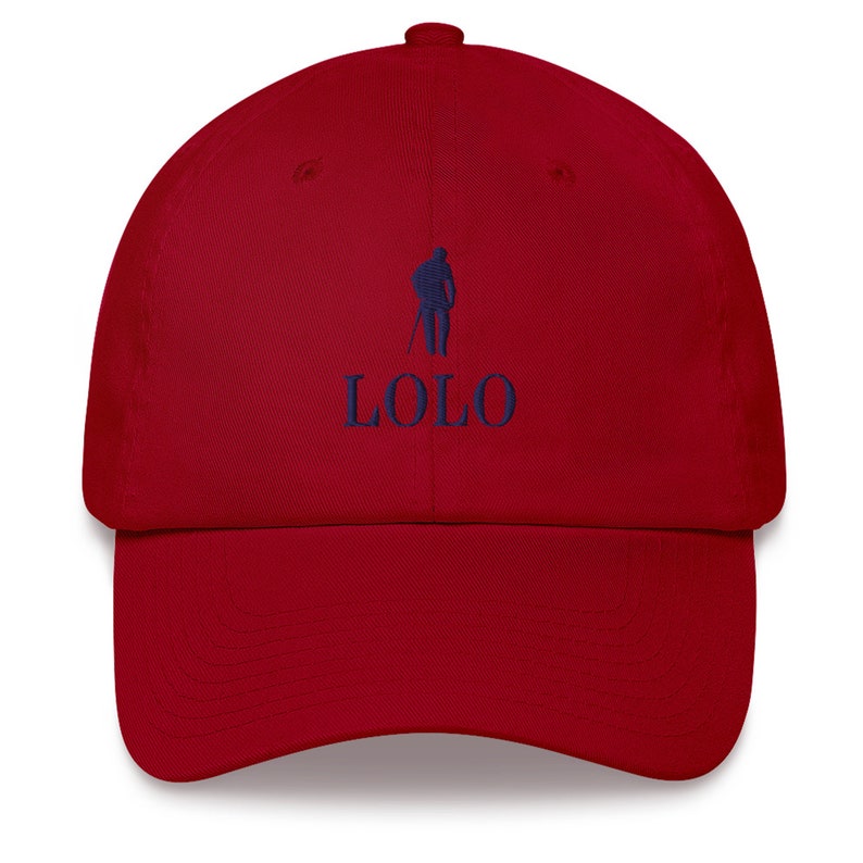 May include: A red baseball cap with a curved brim. The cap features a navy blue embroidered logo of a person with a golf club and the word "LOLO" below it. The cap is made of a soft fabric and has an adjustable strap.