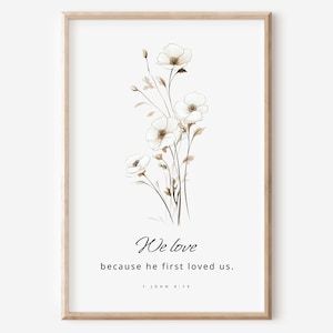 Può includere: Una stampa floreale bianca con una citazione che recita "Amiamo perché lui ci ha amati per primo. 1 Giovanni 4:19"
