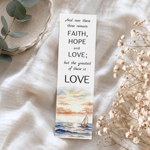 May include: A rectangular paper bookmark featuring black printed text that reads: And now these three remain: FAITH, HOPE and LOVE; but the greatest of these is LOVE. Below the text is a watercolor illustration of a sailboat on the ocean.