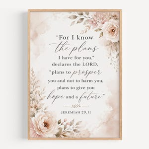 May include: A framed wall art print featuring the Bible verse Jeremiah 29:11 in black serif and script typography. The text is surrounded by watercolour illustrations of soft pink and beige roses, leaves, and sprigs on a white background.