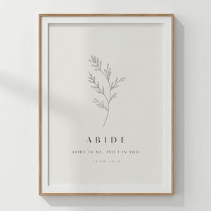 May include: A framed wall art print featuring a minimalist black line drawing of a leafy branch centered above the text ABIDE, followed by the phrase ABIDE IN ME, AND I IN YOU, and the citation JOHN 15:4 in a clean, black serif font on a light background.