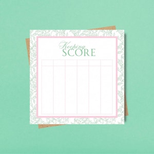 Peut inclure: Un bloc-notes carré avec le texte Keeping SCORE en haut, centré au-dessus d'une grille à six colonnes verticales. Le papier présente un centre blanc, une bordure rose et un motif floral vert clair sur les bords, posé sur une carte brune.