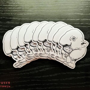 May include: A set of eight white vinyl stickers featuring a cartoon creature with a large head and a small body. The creature has a large eye and a small mouth. The stickers are arranged in a row, with the creature's heads facing the same direction.