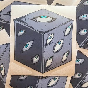 Puede incluir: Un cubo gris con múltiples ojos en cada lado. Los ojos son blancos con iris azules. El cubo está sobre un fondo beige.