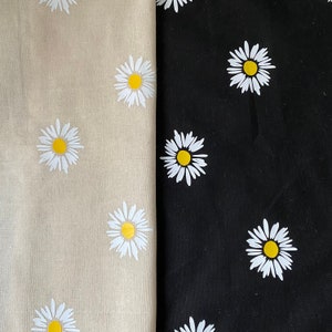 May include: Two fabric swatches with a white daisy pattern. The fabric on the left is beige and the fabric on the right is black.
