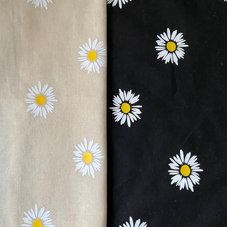 May include: Two fabric swatches with a white daisy pattern. The fabric on the left is beige and the fabric on the right is black.