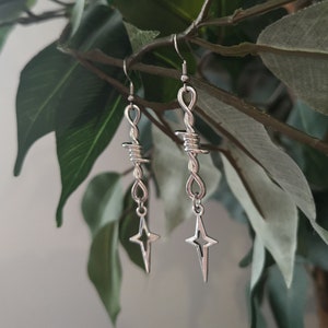May include: A pair of silver earrings with a star charm and a barbed wire design.