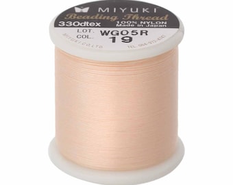 May include: A spool of light peach-colored Miyuki beading thread made of 100% nylon. The label on the top reads 330dtex, 100% nylon, Made in Japan, LOT WG05R, and COL 19. The thread is wound tightly around a white plastic cylindrical spool.