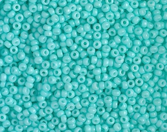 May include: A close-up shot of a large pile of small, round, light blue beads. The beads are uniform in size and shape, with a hole running through the center of each. The beads are scattered, creating a textured surface.