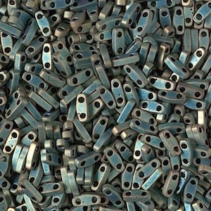 May include: A large pile of teal blue and silver metallic seed beads. The beads are oval shaped with two holes on each side.