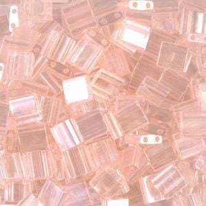 May include: A close-up view of a pile of small, square, translucent pink glass beads. The beads have a subtle iridescent shimmer.