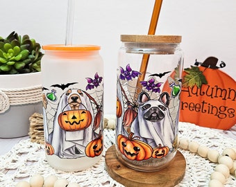 Peut inclure: Deux gobelets en verre avec des motifs d'Halloween. L'un représente un chien déguisé en fantôme tenant une citrouille, l'autre un bouledogue français déguisé en fantôme. Les deux ont des couvercles orange ou en bois et des pailles. Le fond comprend des citrouilles et le texte "Autumn greetings."