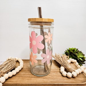 May include: A clear glass tumbler with a bamboo lid and a stainless steel straw. The tumbler has a pink and orange floral design.
