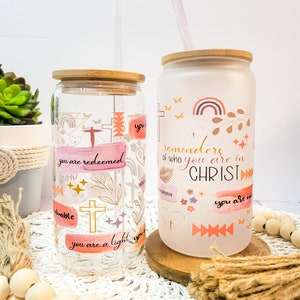 Puede incluir: Dos vasos de vidrio con tapas de madera y pajitas. Los vasos tienen un acabado esmerilado y presentan citas y diseños inspiradores. Las citas incluyen "you are redeemed", "you are a light" y "reminders of who you are in CHRIST".