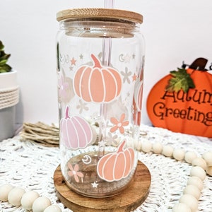 May include: A clear glass tumbler with a bamboo lid and a straw. The tumbler has a fall-themed design with pink and orange pumpkins, stars, and flowers.