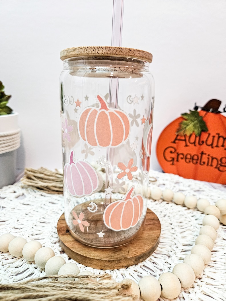 May include: A clear glass tumbler with a bamboo lid and a straw. The tumbler has a fall-themed design with pink and orange pumpkins, stars, and flowers.