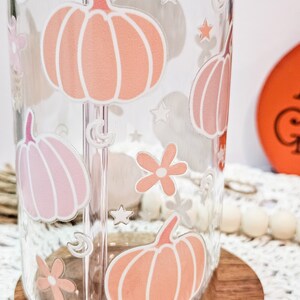 May include: A clear glass water bottle with a straw and a design of pink and orange pumpkins, stars, and flowers.