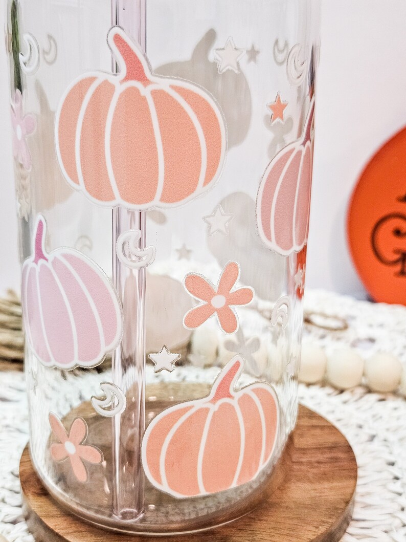 May include: A clear glass water bottle with a straw and a design of pink and orange pumpkins, stars, and flowers.