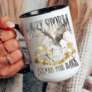 May include: White ceramic mug with a black rim and handle. The mug features a graphic of a dragon with the text "Only Storm The Biggest Battle Yet Brave The Dark".