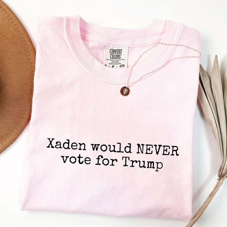 May include: Pink t-shirt with the text "Xaden would NEVER vote for Trump" printed in black.